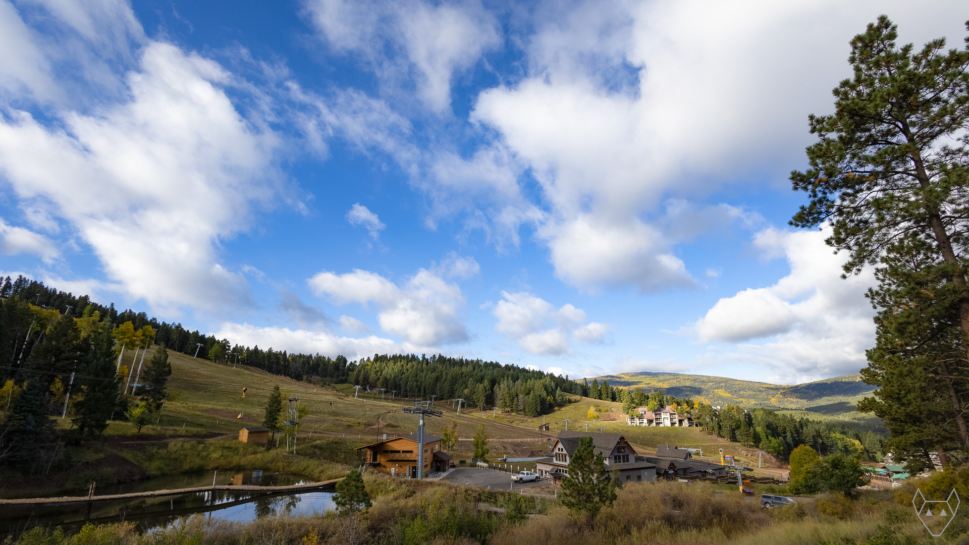 Puffy clouds storm overhead. Their shadows dapple an autumn mountain. A quiet ski resort waits for the snow.