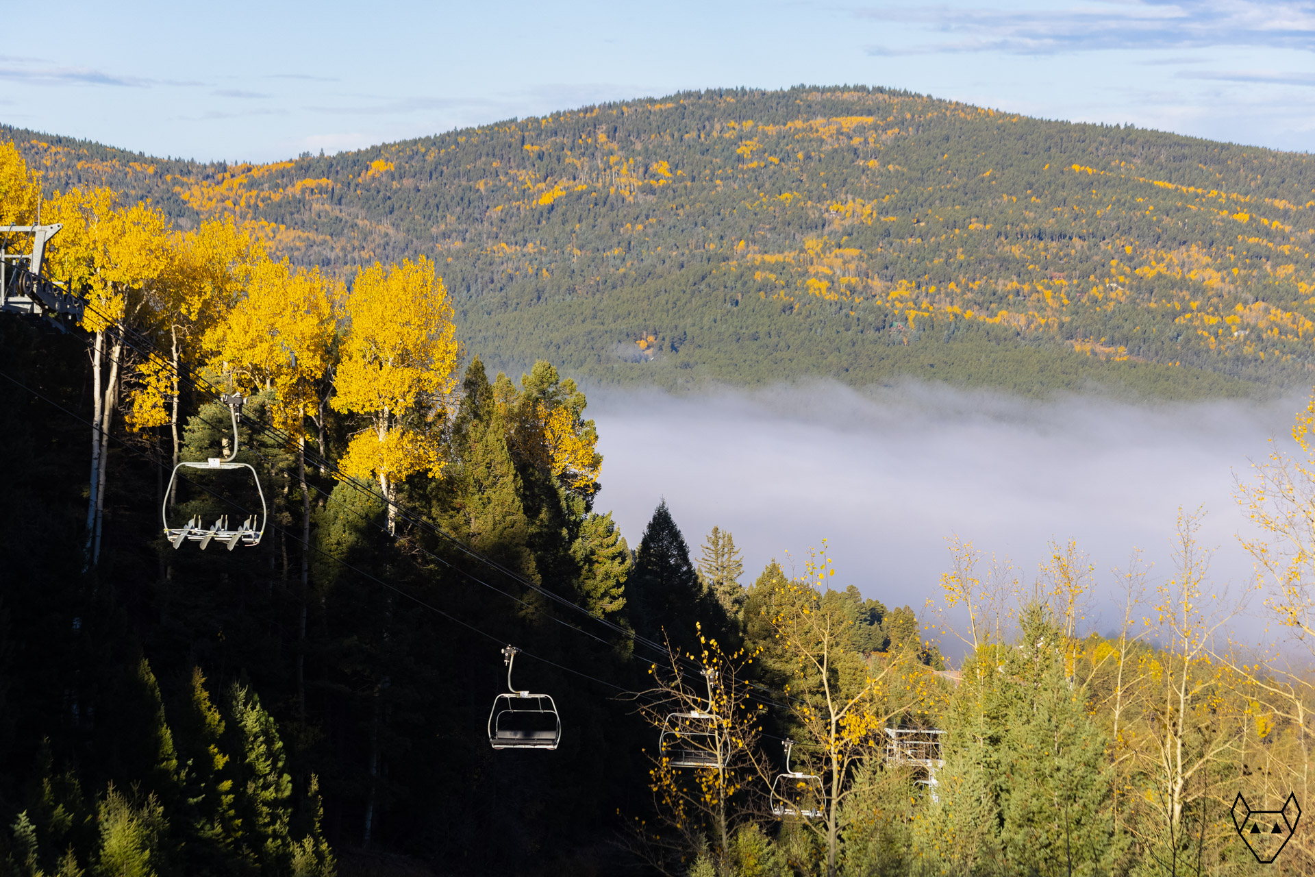 Rocky Mountains ablaze with autumn aspens. Fog covers the valley and the chair lift is closed.